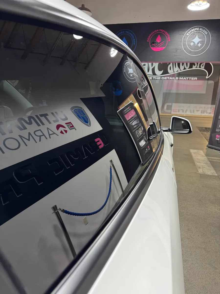 Close view of a tinted rear side window on a white Tesla inside the APC Auto Spa shop
