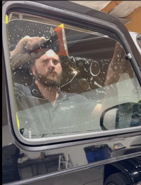 APC Auto Spa installer using a squeegee to smooth window tint film on the inside of a black SUV's front side window